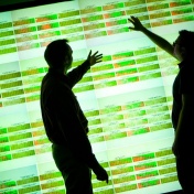 Silhouettes of two men against an illuminated background of big data sets. 
