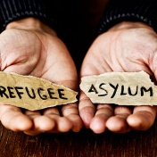 Closeup photo of hands holding scraps of paper reading "Refugee" and Asylum.". 