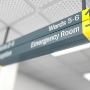 A ceiling mounted hospital directional sign highlighting the way towards the emergency room. 