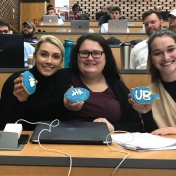 3 sports law students holding cookies shaped like footballs with UB logo on them. 
