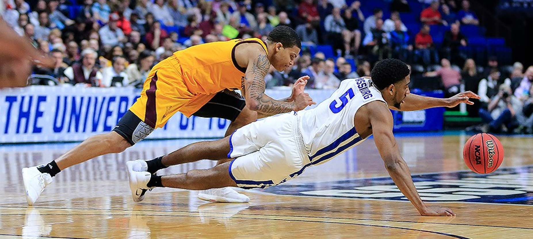 Massinburg holds himself up on one arm, trying to maintain control of the ball as an ASU player tries to steal it away. 