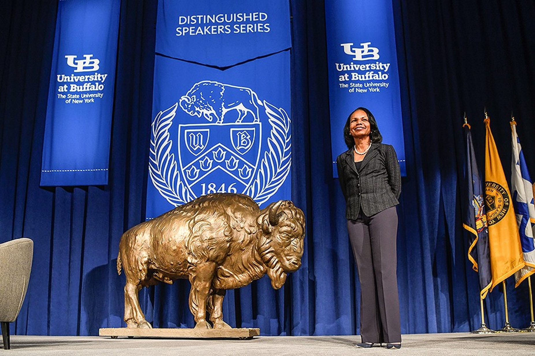 Condoleezza Rice stands on stage next to a golden colored buffalo and under banners that bare the interlocking UB logos, the UB Seal and the words "Distinguished Speakers Series.". 