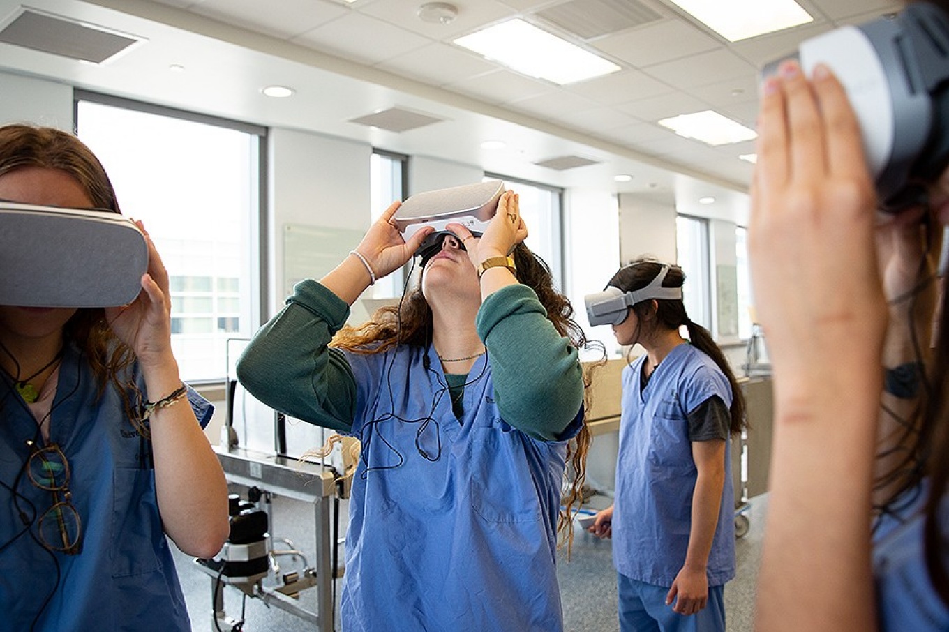 Several medical students in blue scrubs wearing VR goggles. 