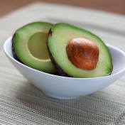 Bowl with two avocado halves, one with the pit. 