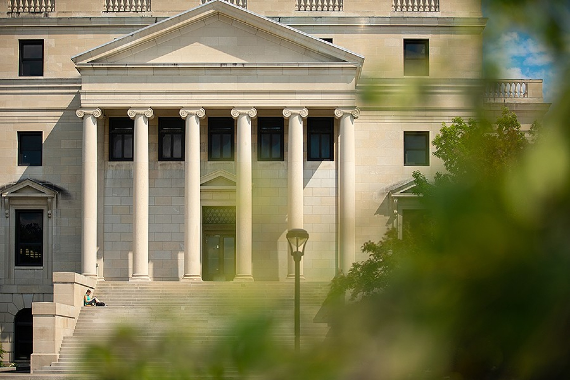A student sits on the stairs of Abbott Library on a summer day.