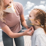 Mother wearing a mask adjusts the mask her young daughter is wearing. 