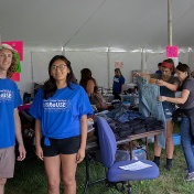 Two people wearing UB ReUSE t-shirts sand in the UB ReUSE sale tent during Welcome Weekend. 
