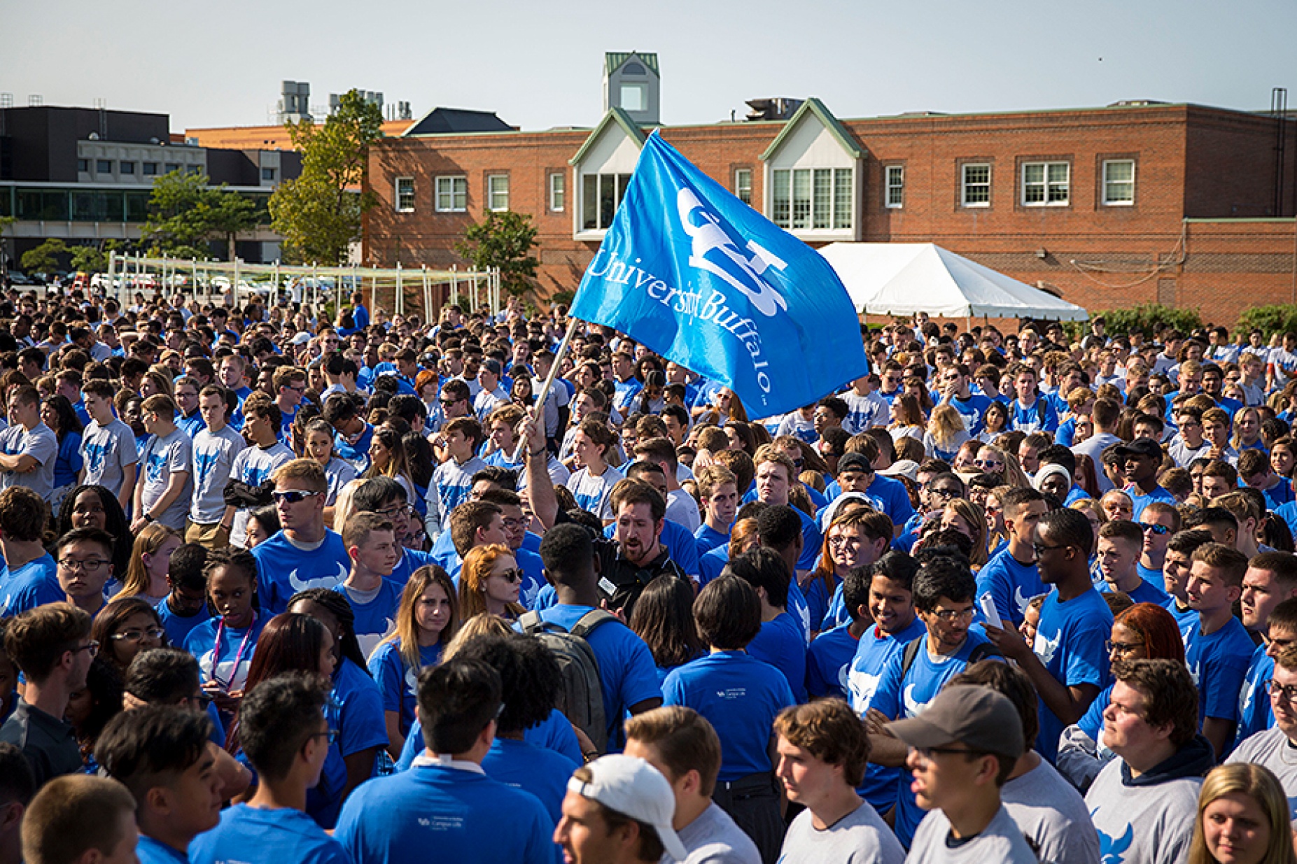 Crowd of students forming the interlocking UB, one waving a UB flag. 