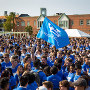 Crowd of students forming the interlocking UB, one waving a UB flag. 