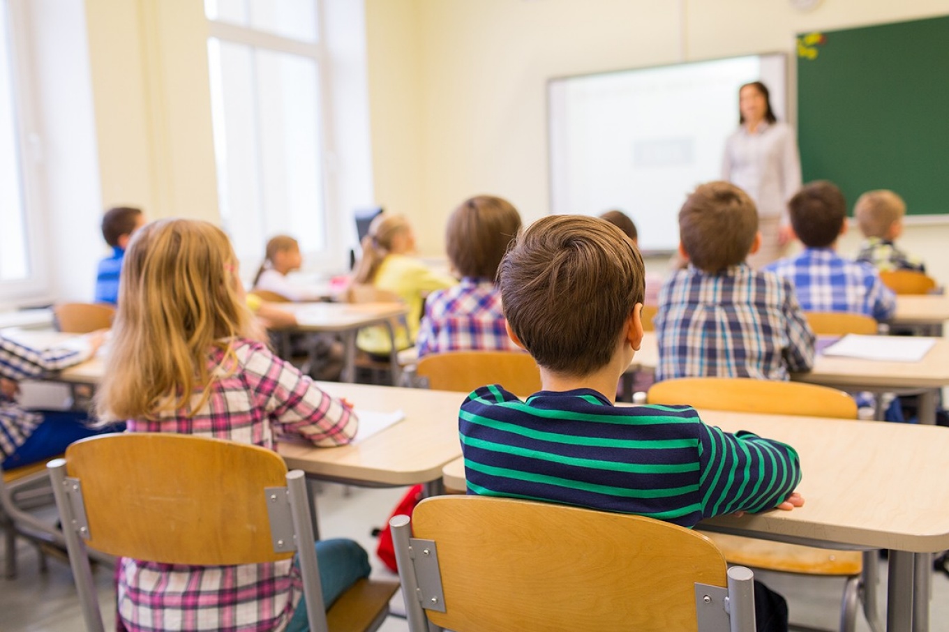 View from the rear of an elementary school classroom to the teacher standing at the front of the room. 