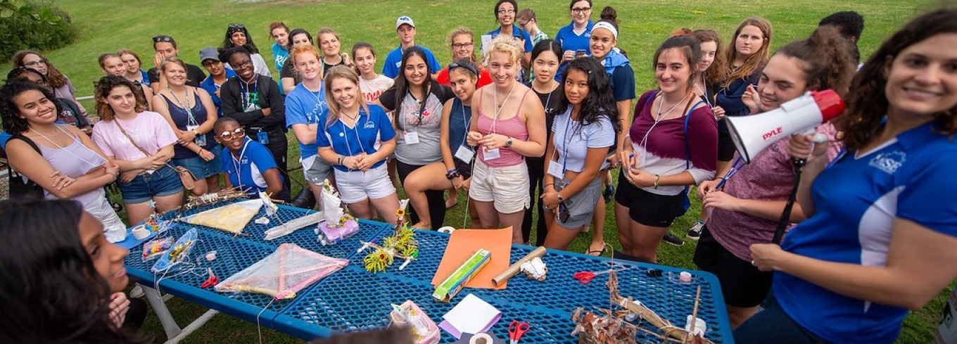 Female freshmen STEM students gathering around an outside table at the early move-in event in 2019. 