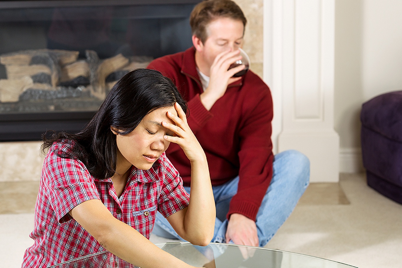 Woman, looking stressed, with alcoholic husband in background. 