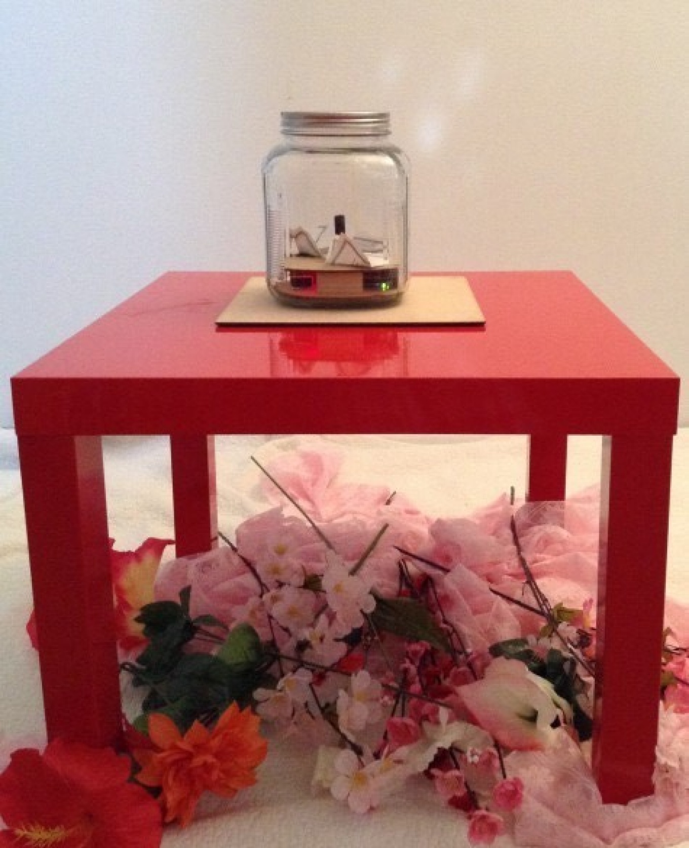 A clear jar filled with scraps of paper sits on a square table.