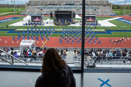 Zoom image: Anne Mecca watches from the box the Jacobs School of Medicine and Biomedical Sciences’ commencement on April 30, looking for details, such as how the rows of students are dismissed. 