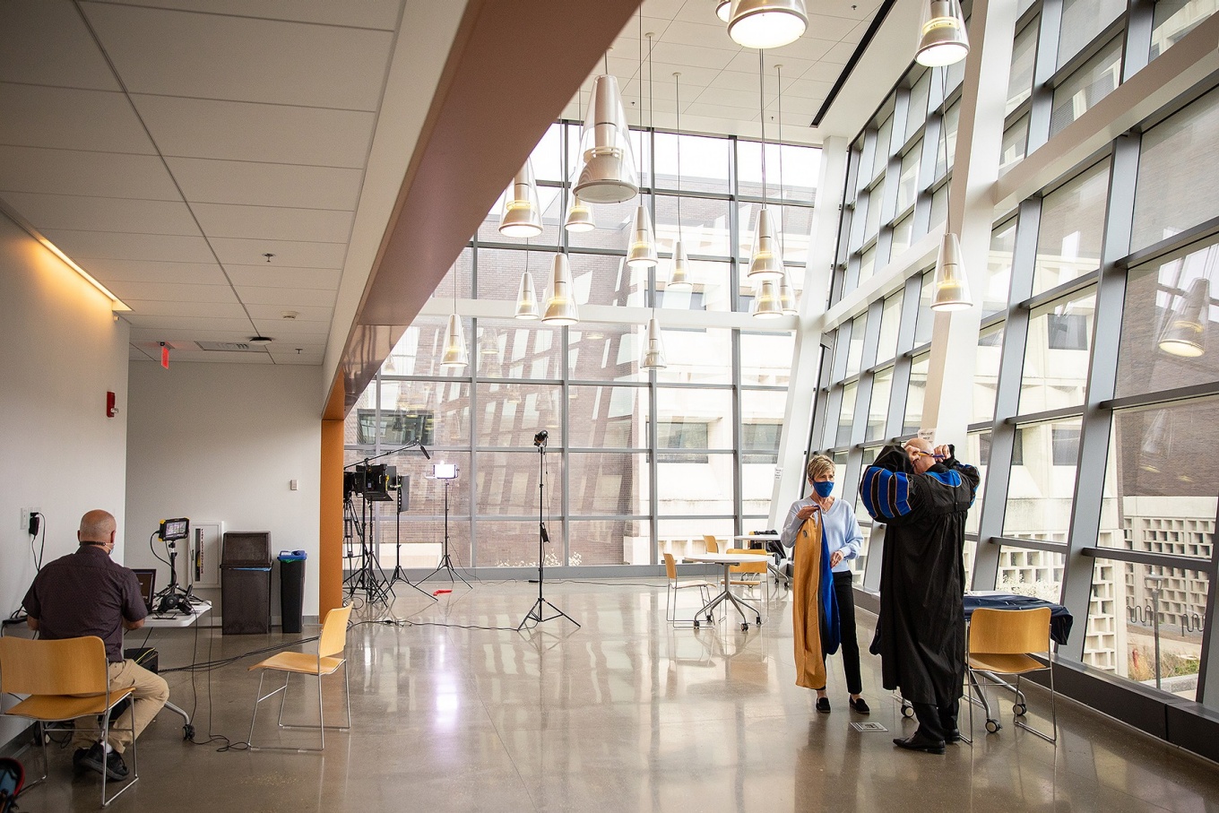 Zoom image: Regina Ticco helped SEAS Dean Kemper Lewis don his regalia before recording his commencement message from the Davis Hall atrium on April 16. Paul Calandra (left) prepared to run the teleprompter. 