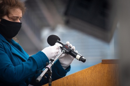 Zoom image: A team member from Event Planning and Services wipes down a microphone at the podium during the Jacobs School commencement ceremony. 
