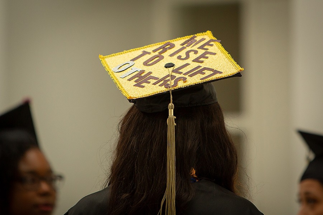 An ALANA graduate wearing a cap that reads, "We rise to lift OThers.". 
