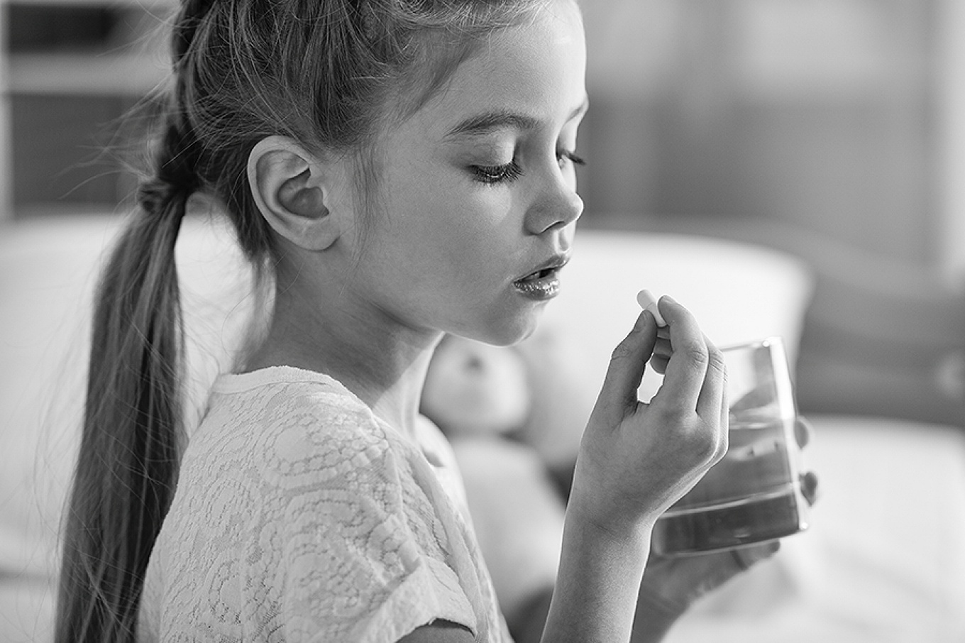 A young girl taking a pill with a glass of water. 