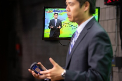 Zoom image: The monitor at the side of the green screen shows Lam what the audience at home is seeing during his weather report. Photo: Meredith Forrest Kulwicki 