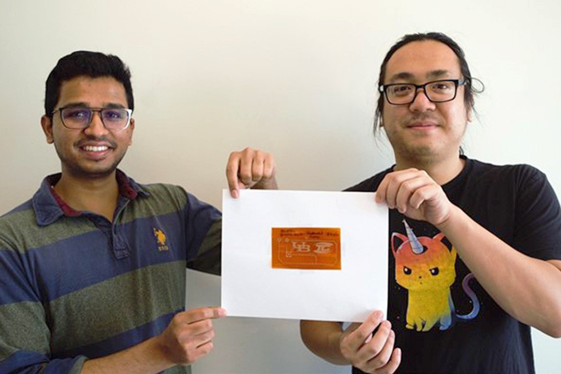 UB graduate research assistant Saurabh Khuje (left) and postdoctoral researcher Aaron Sheng, PhD, hold an example of flexible hybrid electronic device that was printed using a copper ink material. 