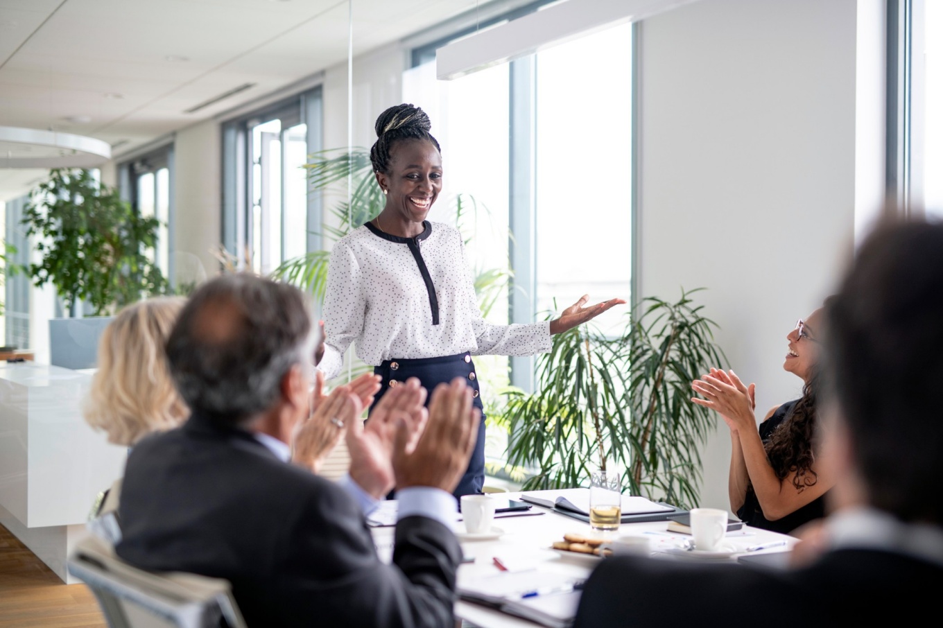 Smiling woman gesturing to colleagues seated at a conference table. 