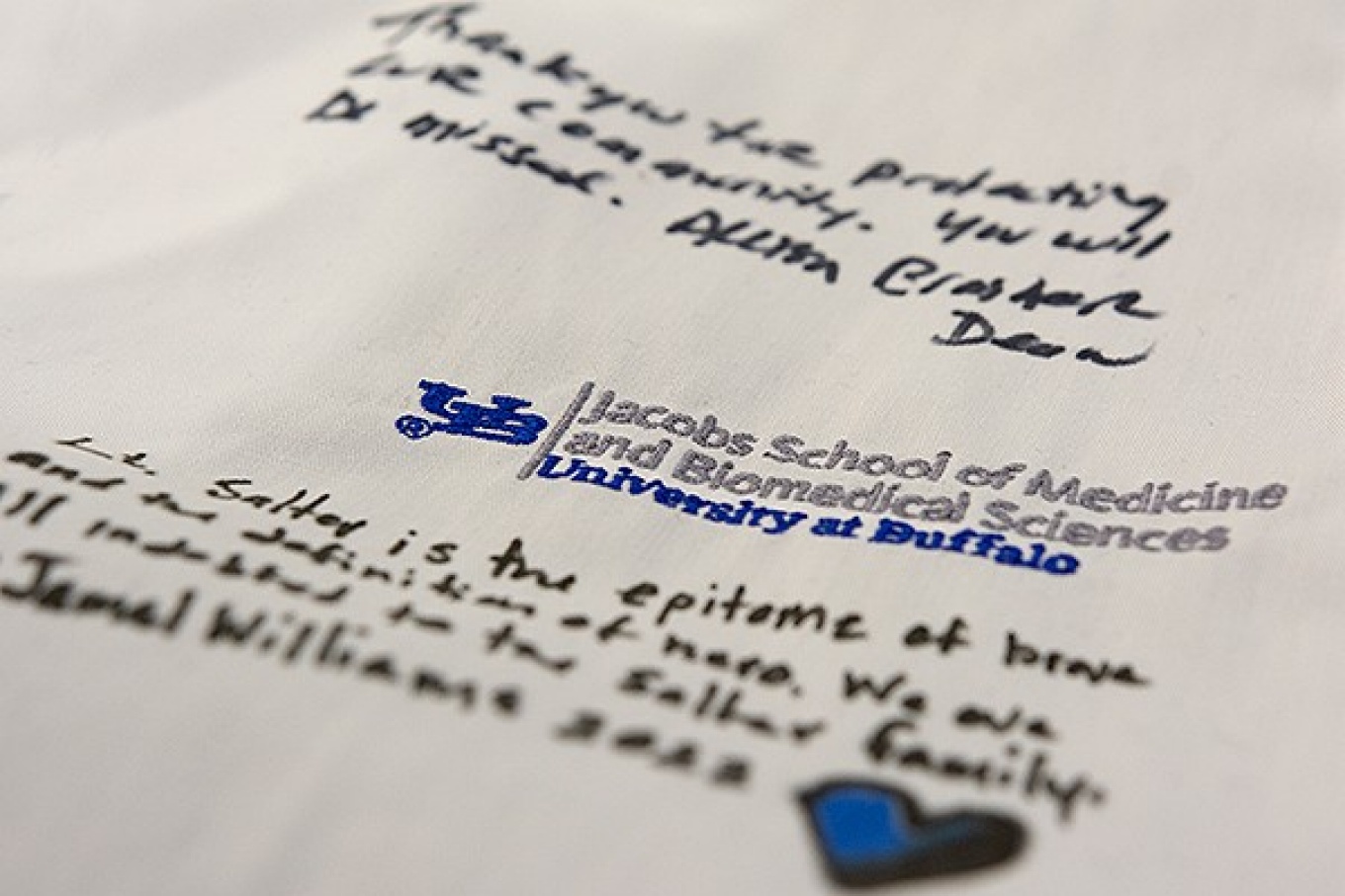 Detail of a medical white coat signed bu students and faculty of the Jacobs School of Medicine and Biomedical Sciences honoring Tops hero Lt. Aaron Salter. 