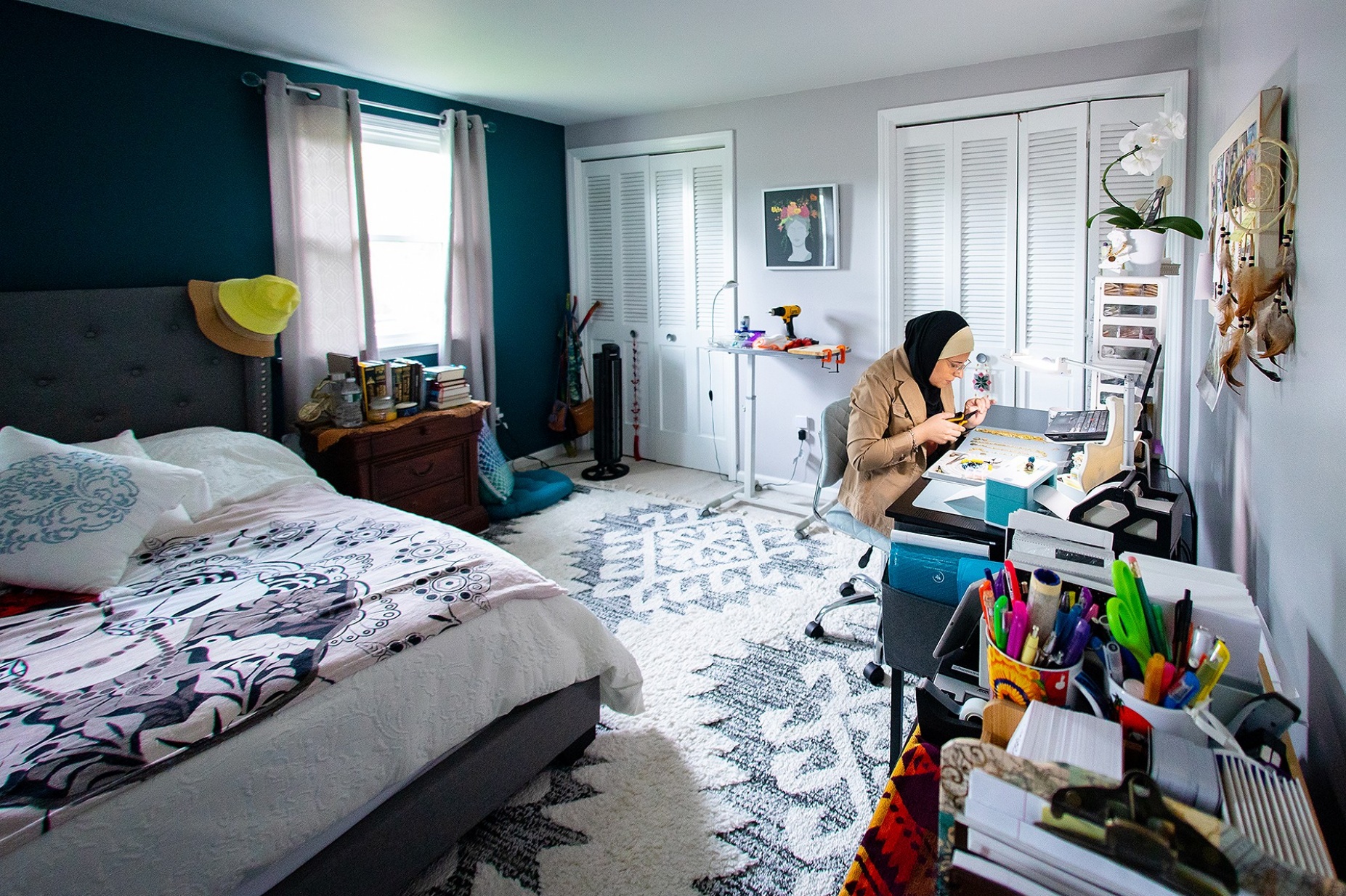 Zoom image: Aref's current workspace is in her personal bedroom at her Williamsville home. She has all her supplies at hand, organized in containers and binders. The bookshelf also holds her packaging and shipping supplies. 