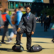A. J. Franklin standing with one foot on a boombox while students pass by. 