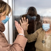 A person visits their elderly relative through a glass door during the Covid-19 pandemic. 