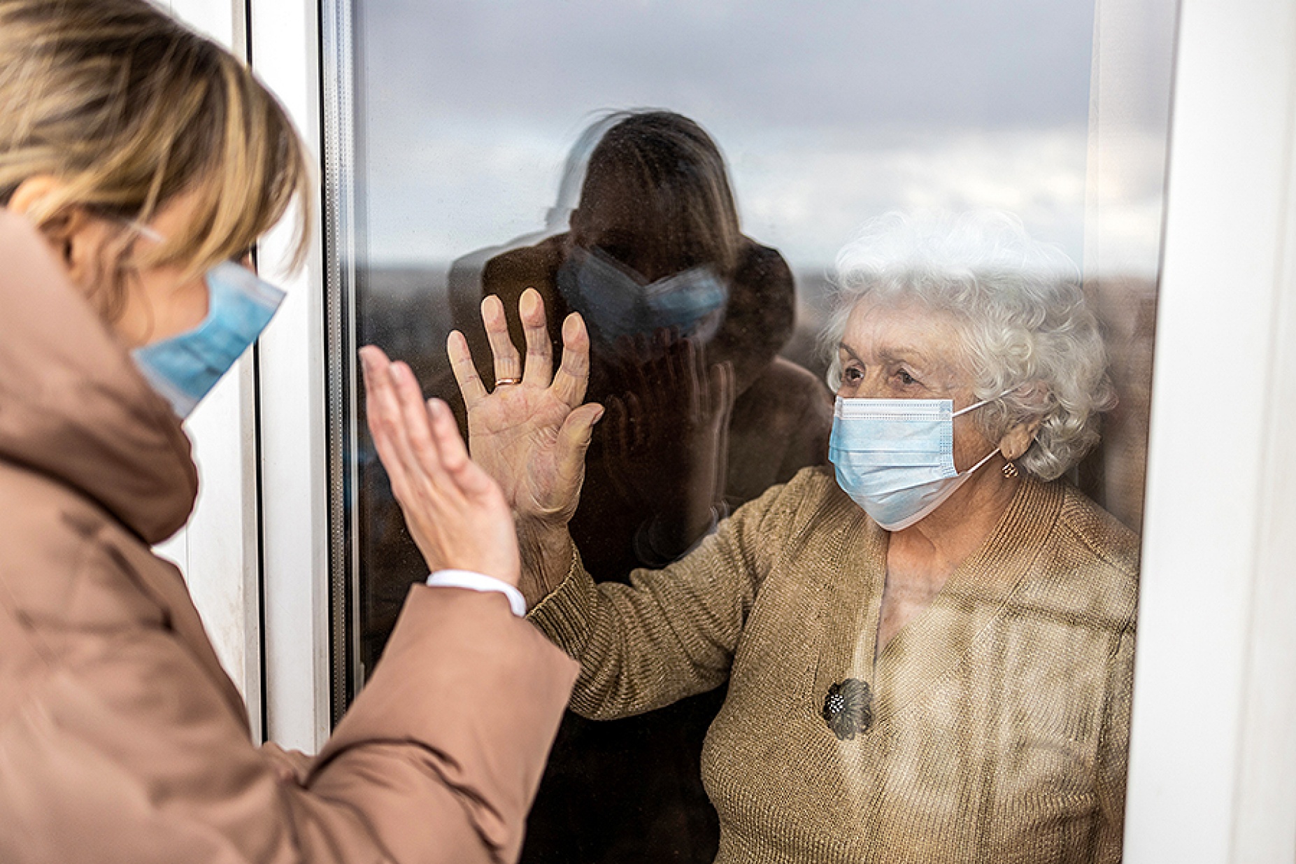A person visits their elderly relative through a glass door during the Covid-19 pandemic. 