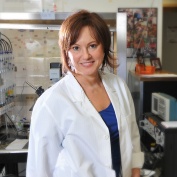 Gabriela Popescu in white coat standing in her lab. 