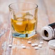 Bottle of spilled pills, glass of alcohol on a table. 