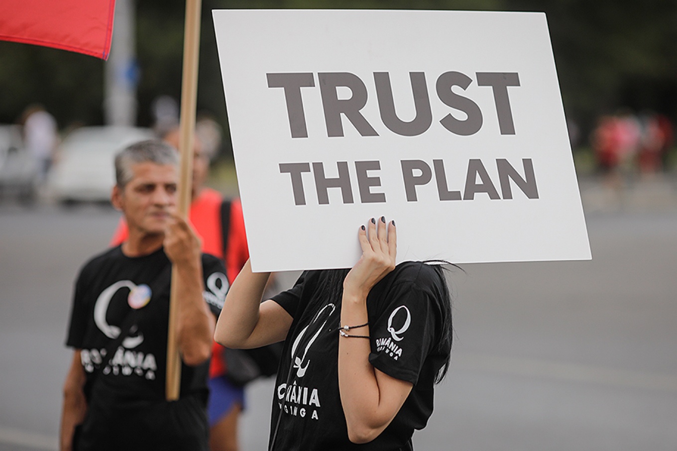 Person holding a sign reading Trust the Plan. 