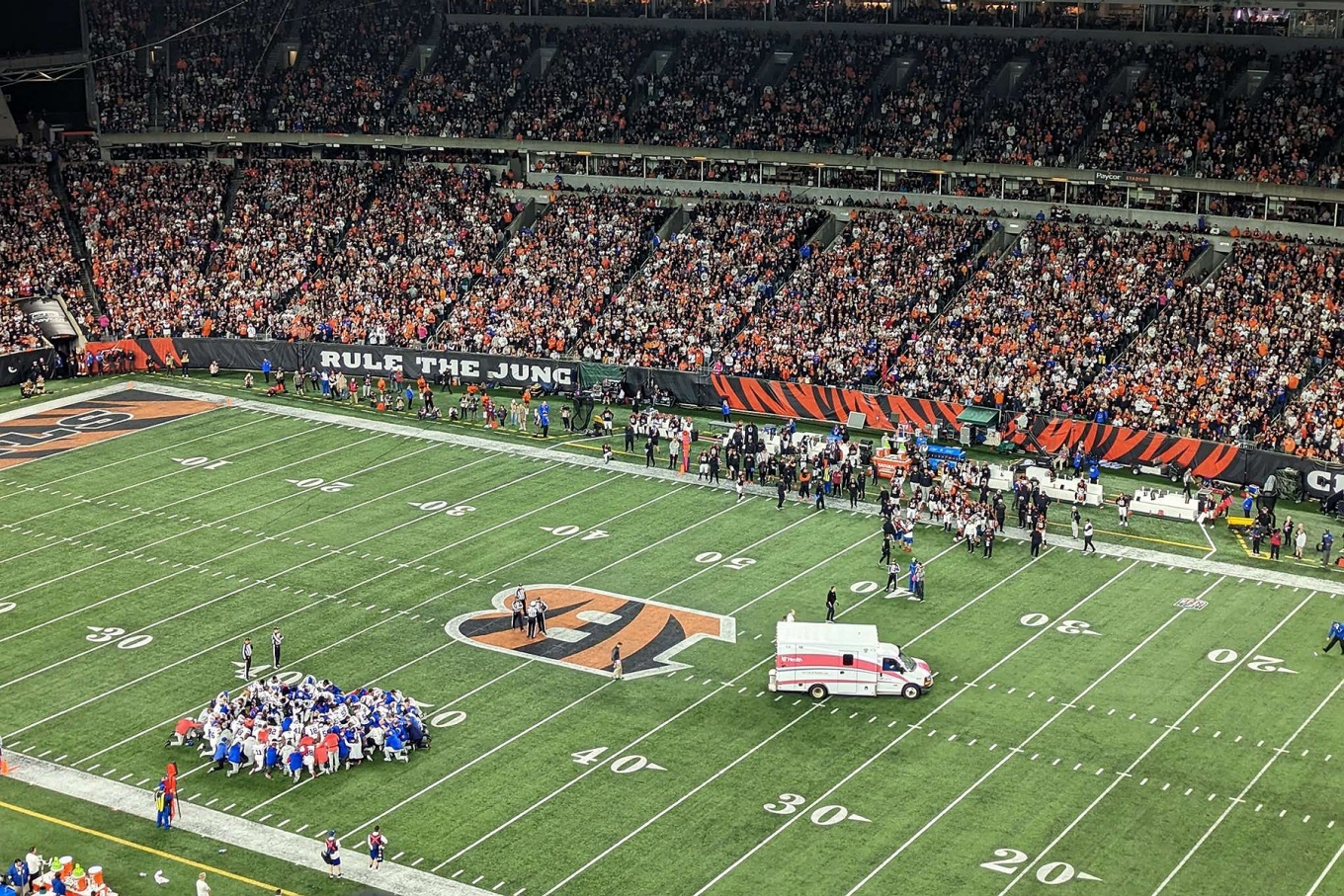 Buffalo Bills Safety Damar Hamlin is removed from Paycor Stadium in Cincinnati, Ohio in an ambulance. The Buffalo Bills, in white, kneel at the bottom left of the image.