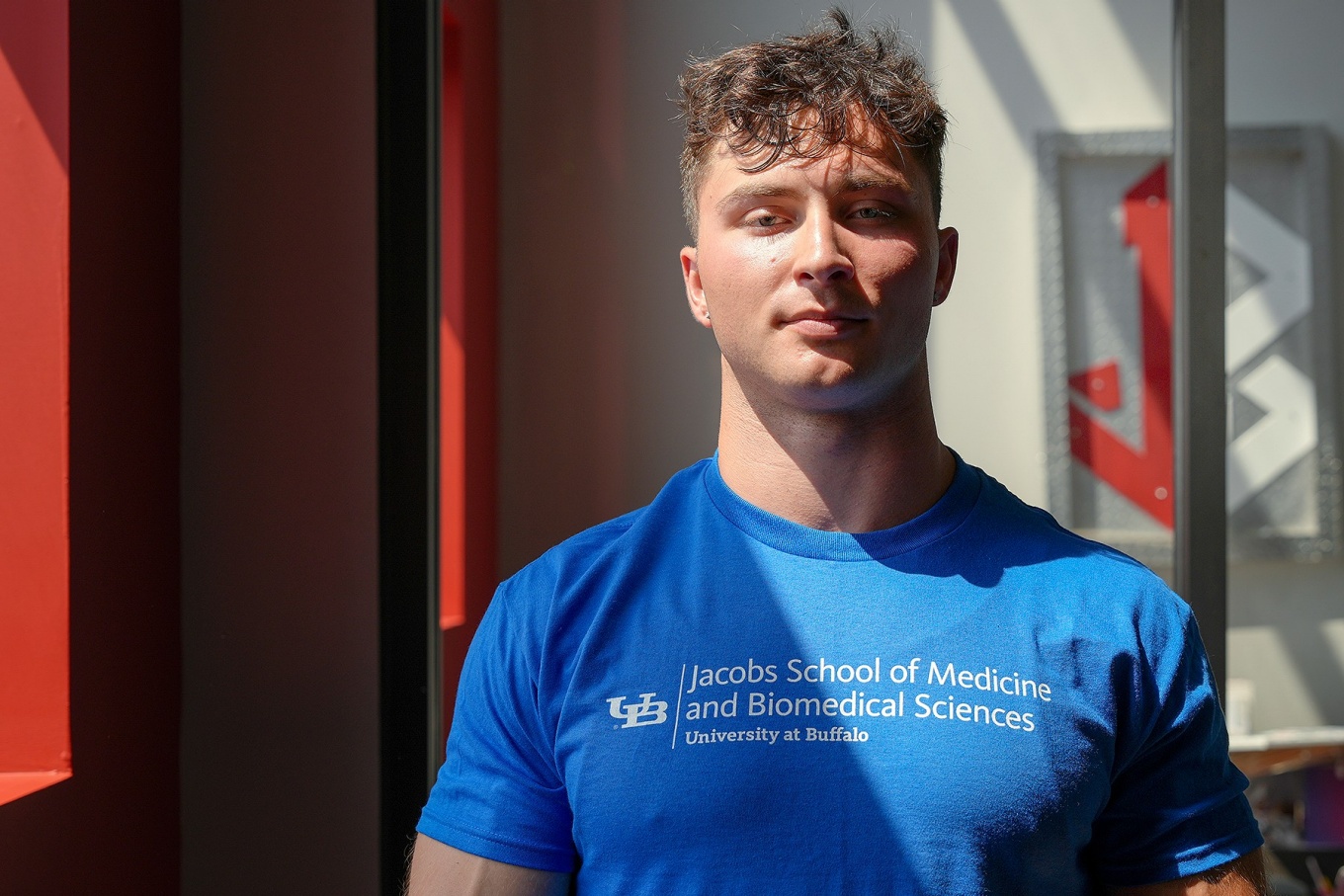 John Taylor wearing a UB blue Jacobs School of Medicine and Biomedical Sciences t-shirt. 