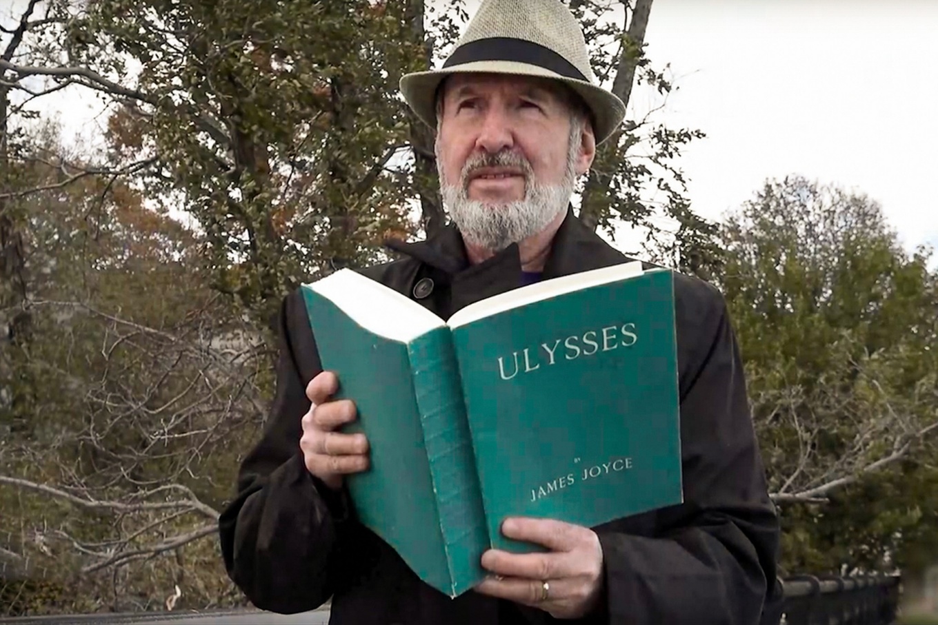 Joyce scholar Michael Groden pictured outdoors holding an open copy of "Ulysses" by James Joyce. 