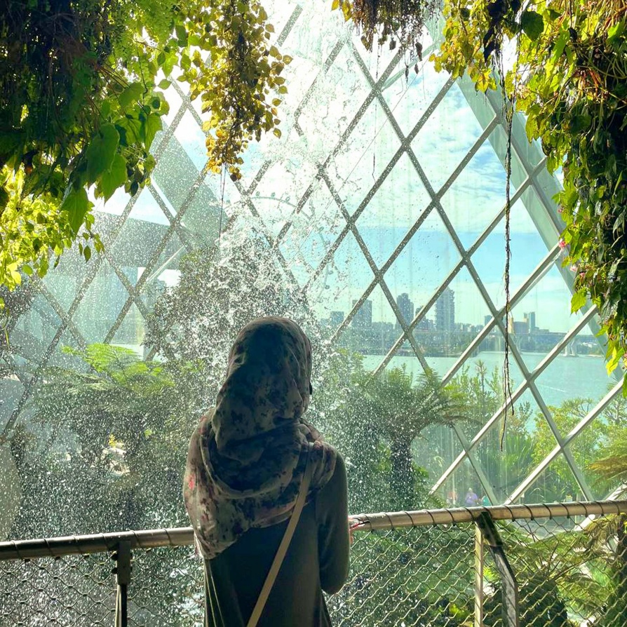 A woman wearing a head scarf looking out over a body of water at a large cosmopolitan city.