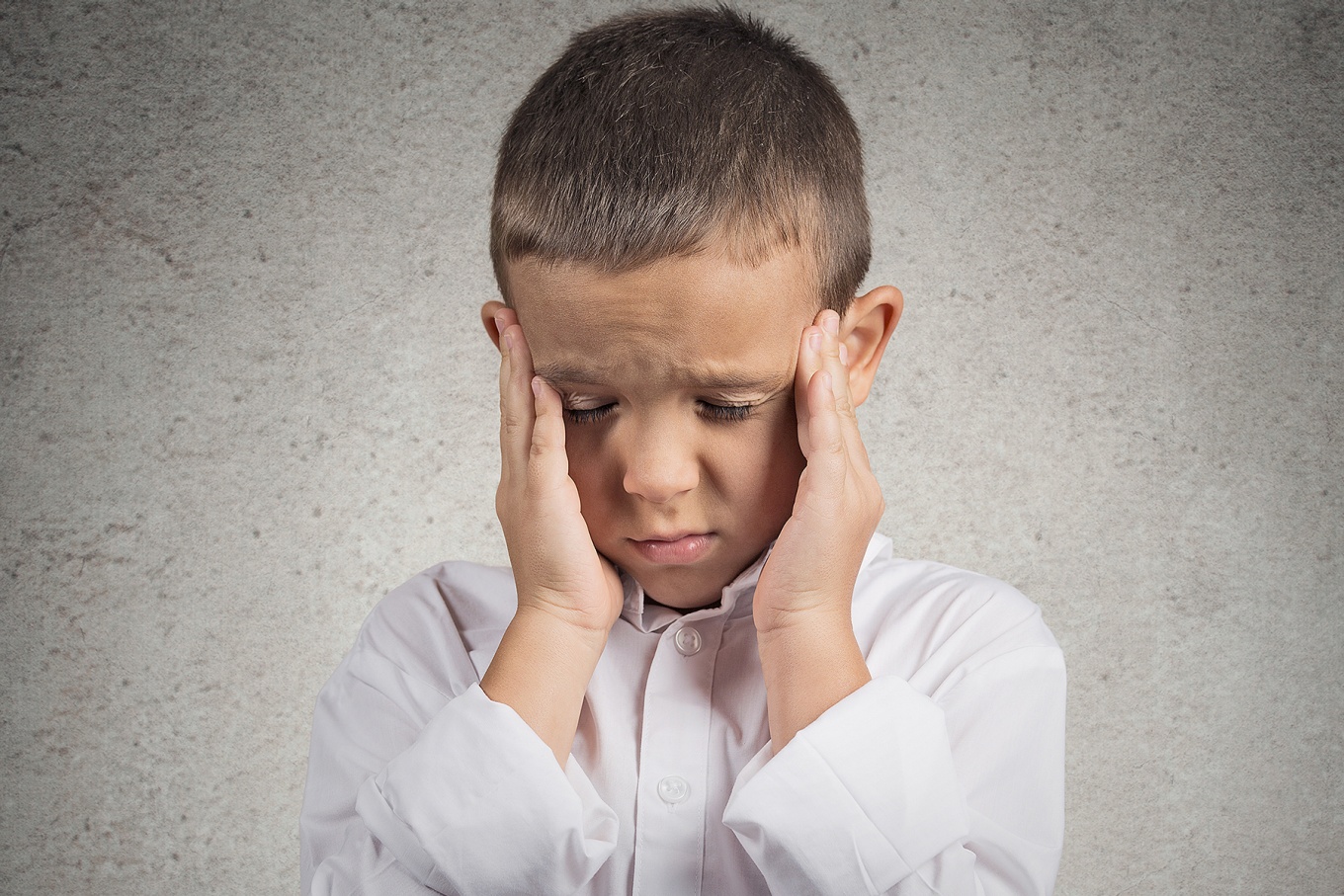Child with eyes closed rubs his temples. 