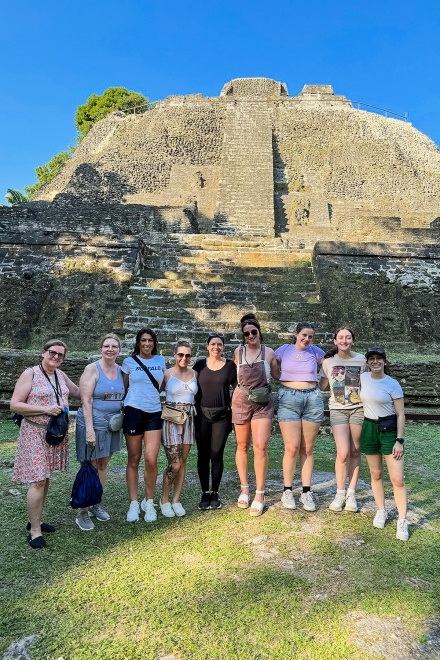 Zoom image: From left, Linda Paine Hughes, Gail Bain Markowski, Caitlyn Tiedemann, Emily Gaghich, Molli Oldenburg, Rena Kessel, Sophia Justo, Emily Pandel and Skylar Bard at Mayan ruins in Belize. 