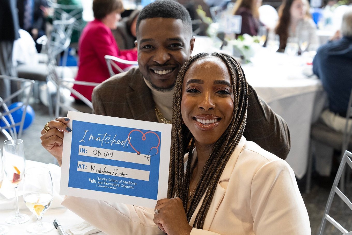 A medical School student holds up a sign stating the field and institution they matched with. 