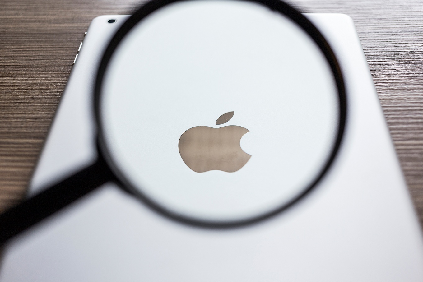 A magnifying glass focused on the Apple logo on an iPad. 