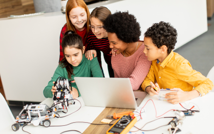 A teacher and students use a computer together to work on a robotics project. 