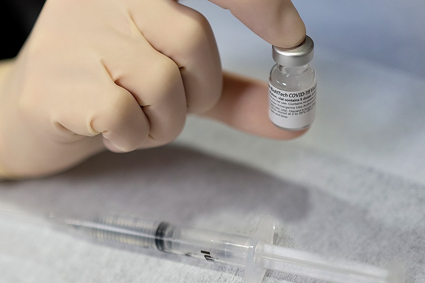 Hand holding a vaccine vial, with syringe. 