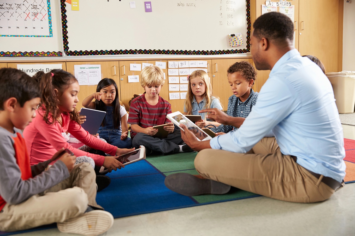 A teacher and students seated on the floor, each with a tablet. 