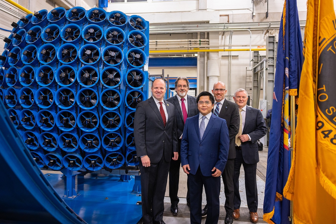 Several people pose together near a fan array for a wind tunnel. 