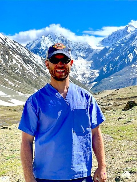 Shawn Vainio pictured wearing scrubs while in a remote area with a mountain range in the background. 