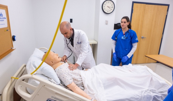 Zoom image: UB nursing student Brianna Churakos (right) watches as simulation coordinator James Cozza checks a "patient's" vital signs during a simulation exercise in May 23 in Wende Hall. Photo: Douglas Levere 