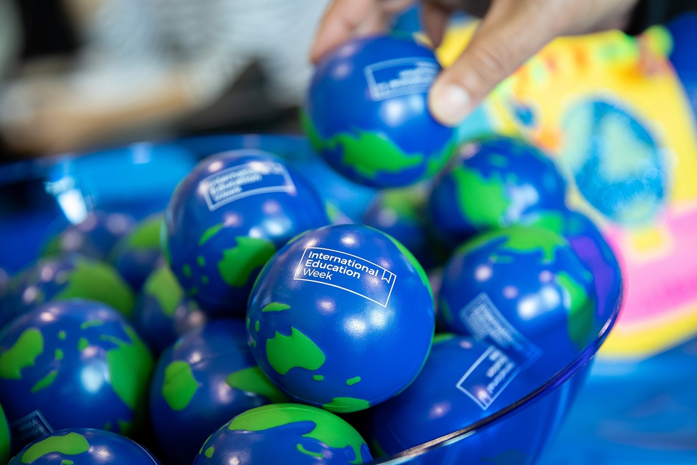A bowl full of stress ball that look like the planet Earth and include the worlds, "International Education Week.". 