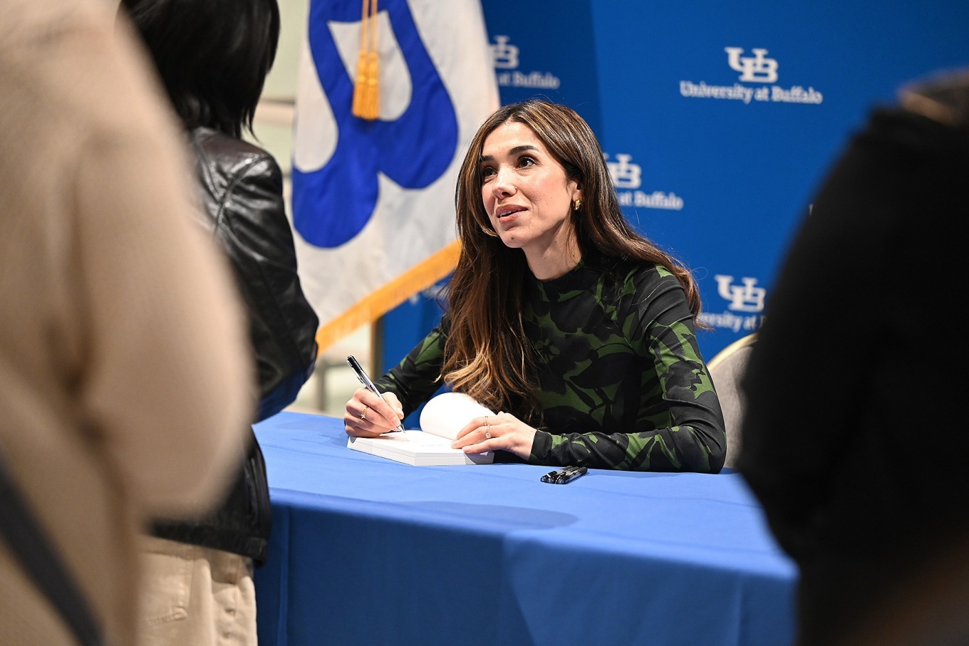 Nadia Murad seated at a table signs books for audience members. 