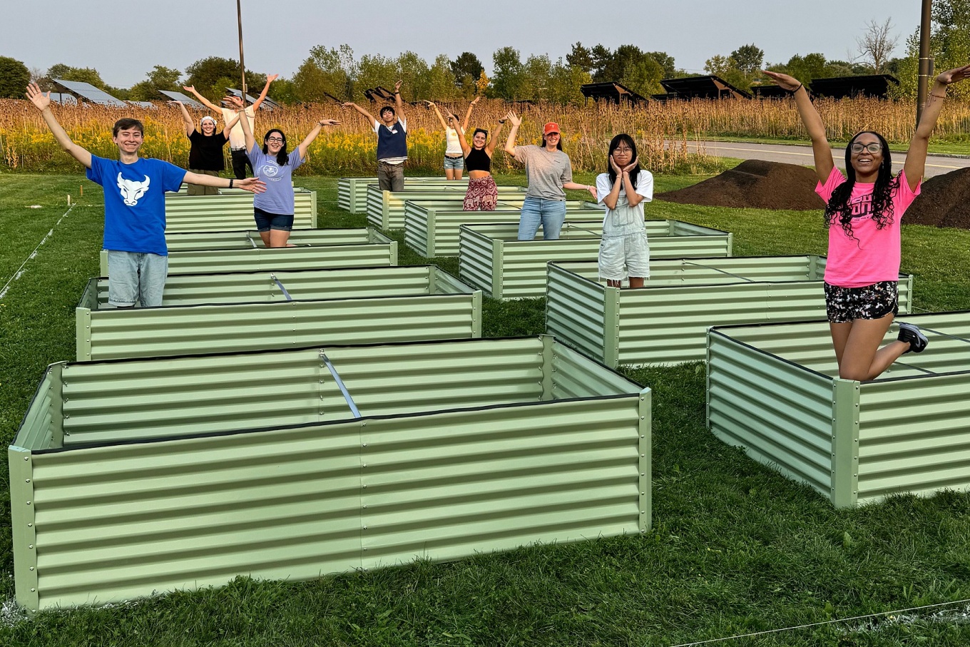 Students standing in raised garden bed frames raise their arms exuberantly.